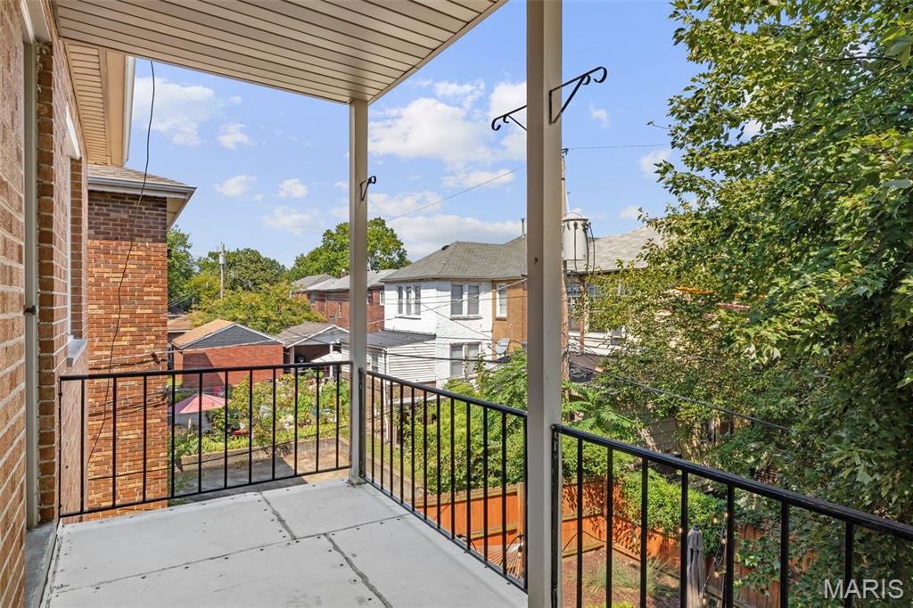 Covered balcony with black railings overlooking leafy trees and neighboring homes.