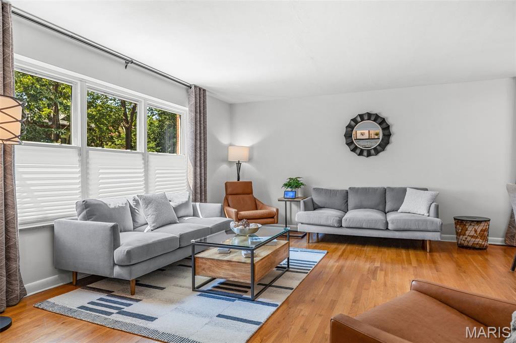 Living room with gray sofas, a leather accent chair, and large windows overlooking leafy trees.