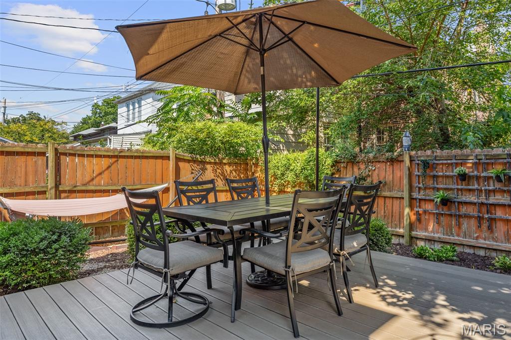 Raised deck with a dining table under a large umbrella and a hammock beside the wooden fence.