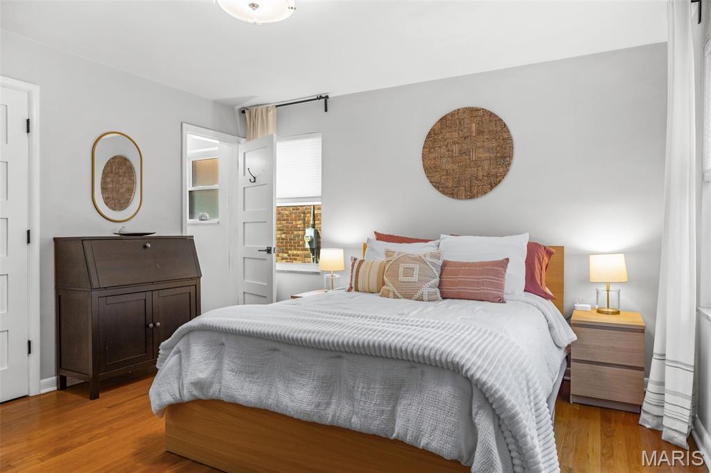 Bedroom with a wooden bed, terracotta accent pillows, hardwood floors, and a dark wooden cabinet.