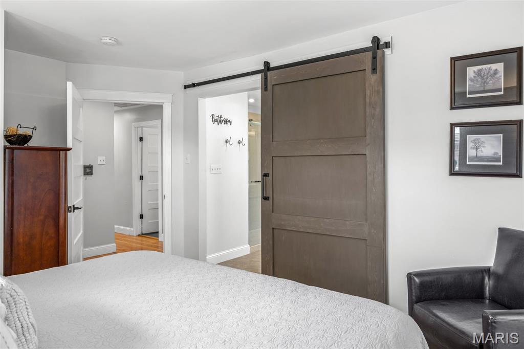 Bedroom with a white bed, sliding barn door, and doorway to the bathroom.