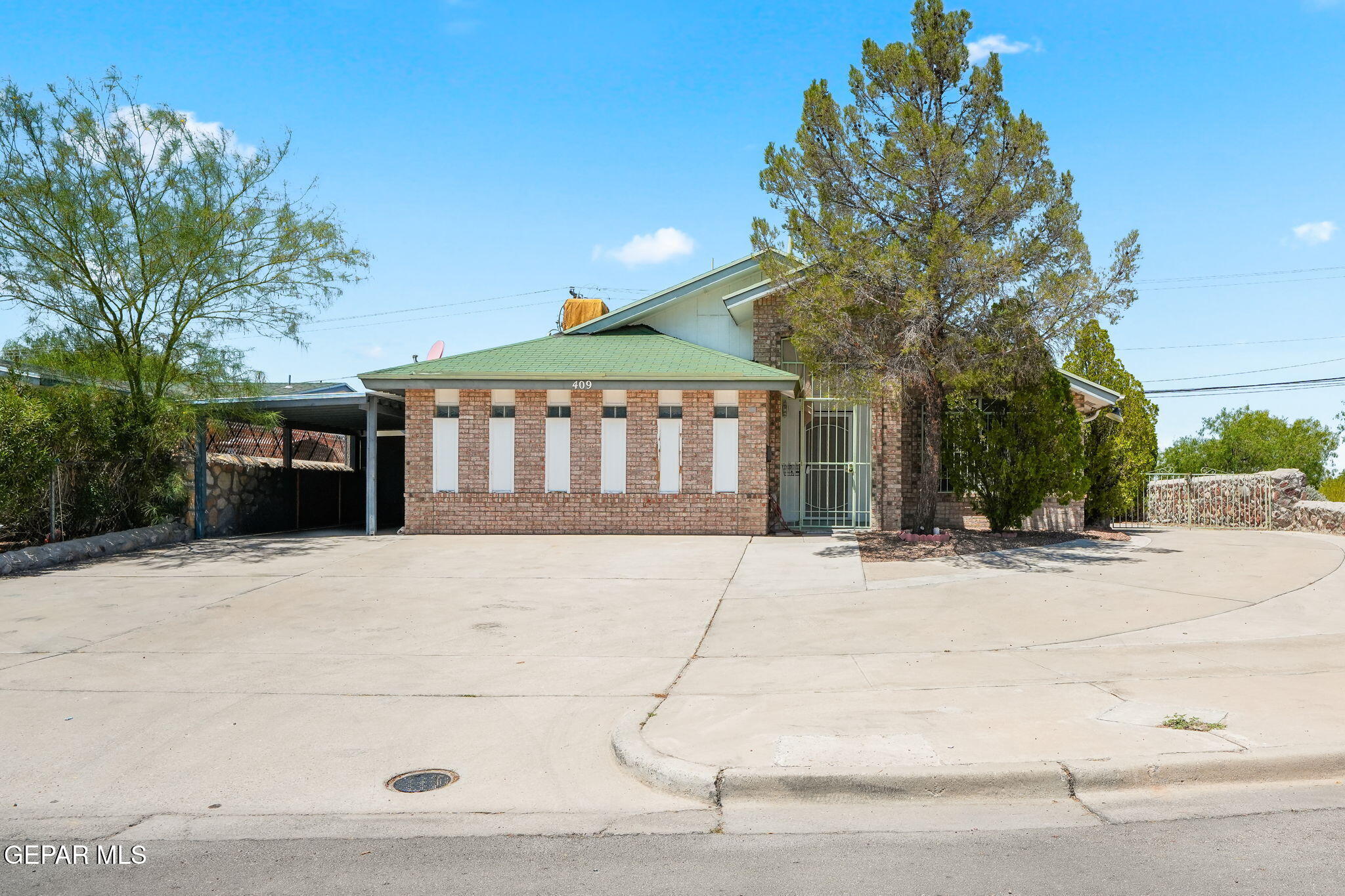 Brick property with a green roof, gated entrance, and broad concrete driveway.