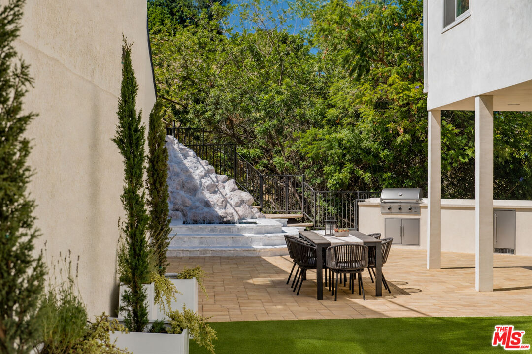 Paved patio with outdoor dining set, built-in grill, and landscaped rock feature.