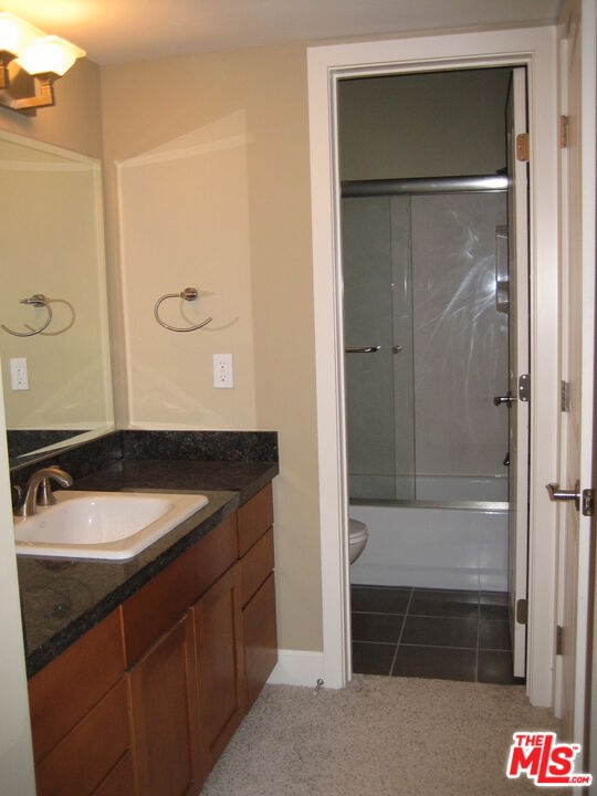 Bathroom vanity with a white sink and dark countertop beside an open doorway to a glass-enclosed tub and shower.