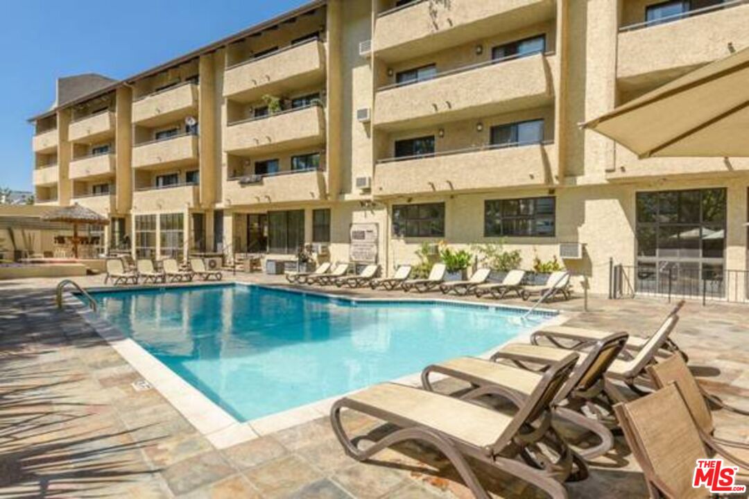 Apartment building pool with lounge chairs on a stone-paved deck.