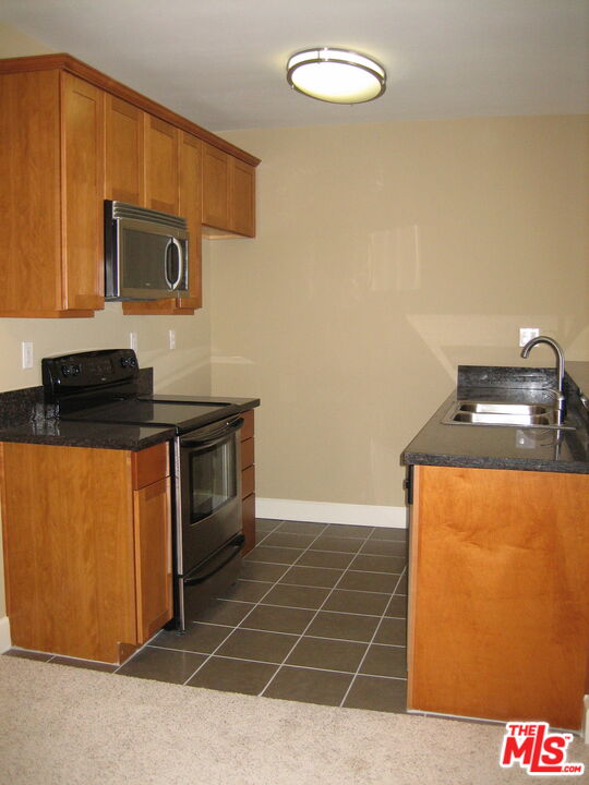 Vacant kitchen with wood cabinets, dark countertops, built-in microwave, electric range, and tiled floor.