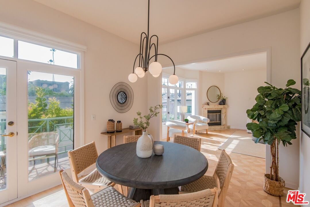 Dining area with a round table and woven chairs opening to a sunlit living room with fireplace.