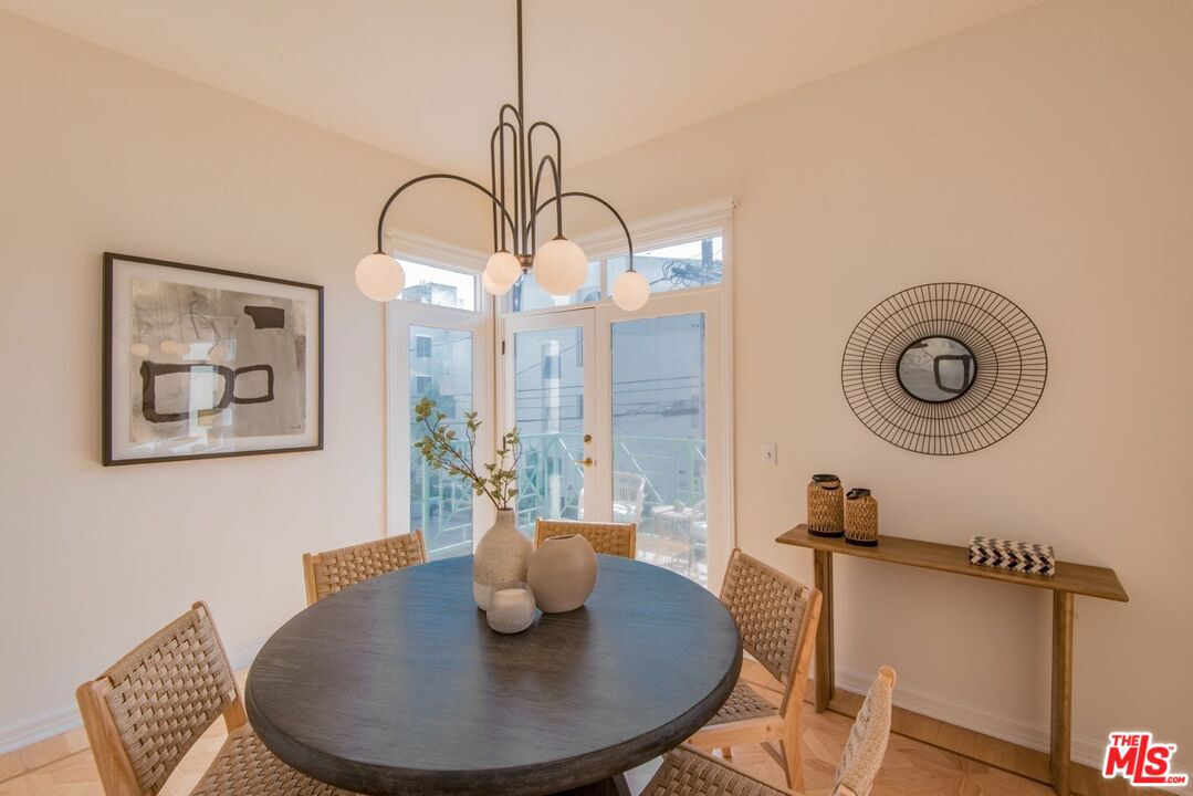 Dining room with a round table, woven chairs, sculptural pendant light, and corner balcony doors.