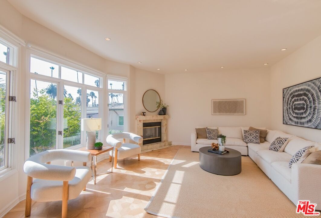 Bright living room with tall windows, a stone fireplace, and white seating.