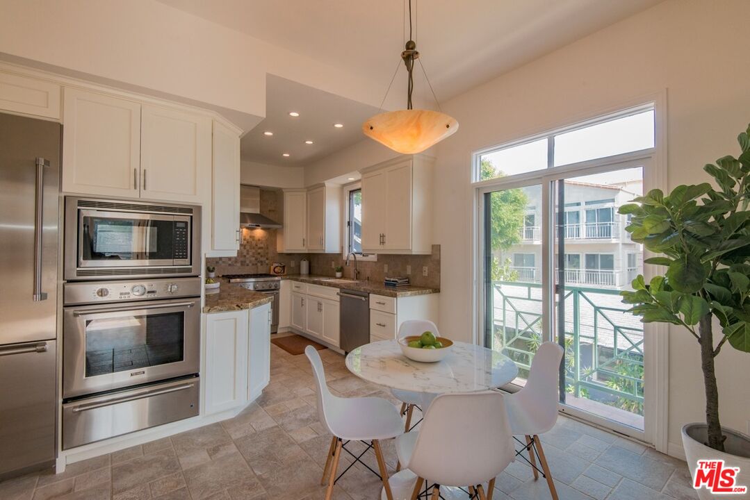 Kitchen with white cabinets, stainless steel appliances, and a round dining table beside balcony doors.