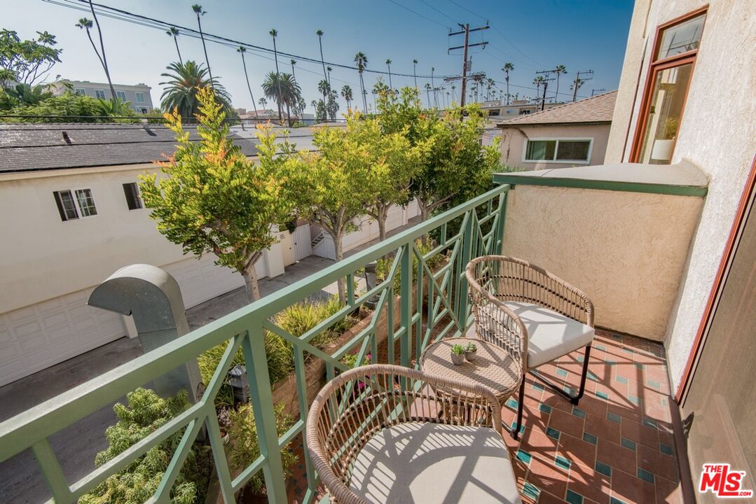 Apartment balcony with wicker seating, patterned tile flooring, and a view of trees and neighboring buildings.