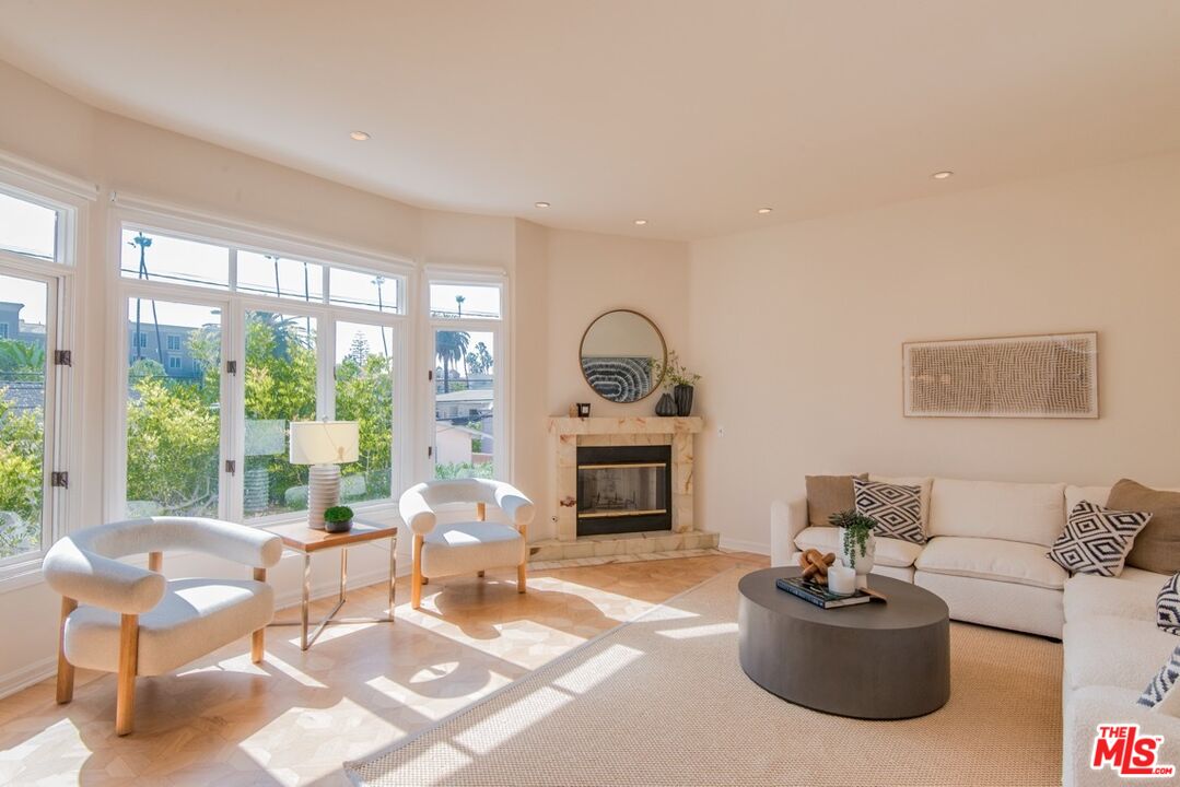 Bright living room with large windows, marble fireplace, cream sectional, and two accent chairs.