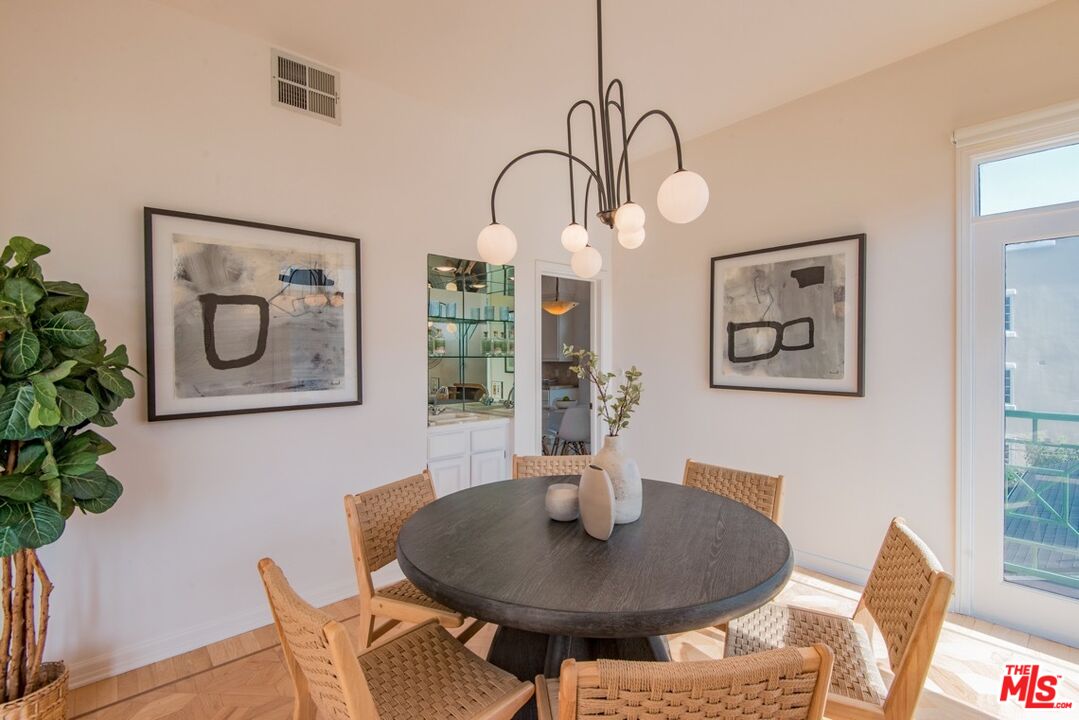 Dining room with a round table, woven chairs, sculptural pendant light, and balcony doors.