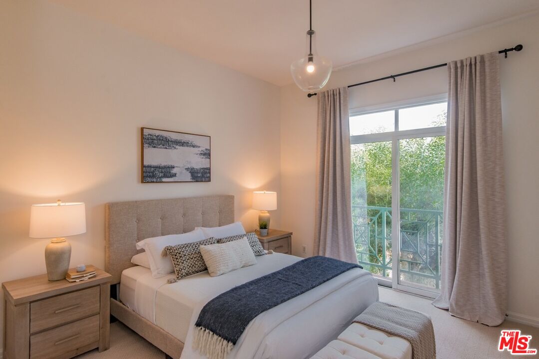 Bedroom with a tufted headboard, white bedding, and a curtained glass door overlooking leafy greenery.