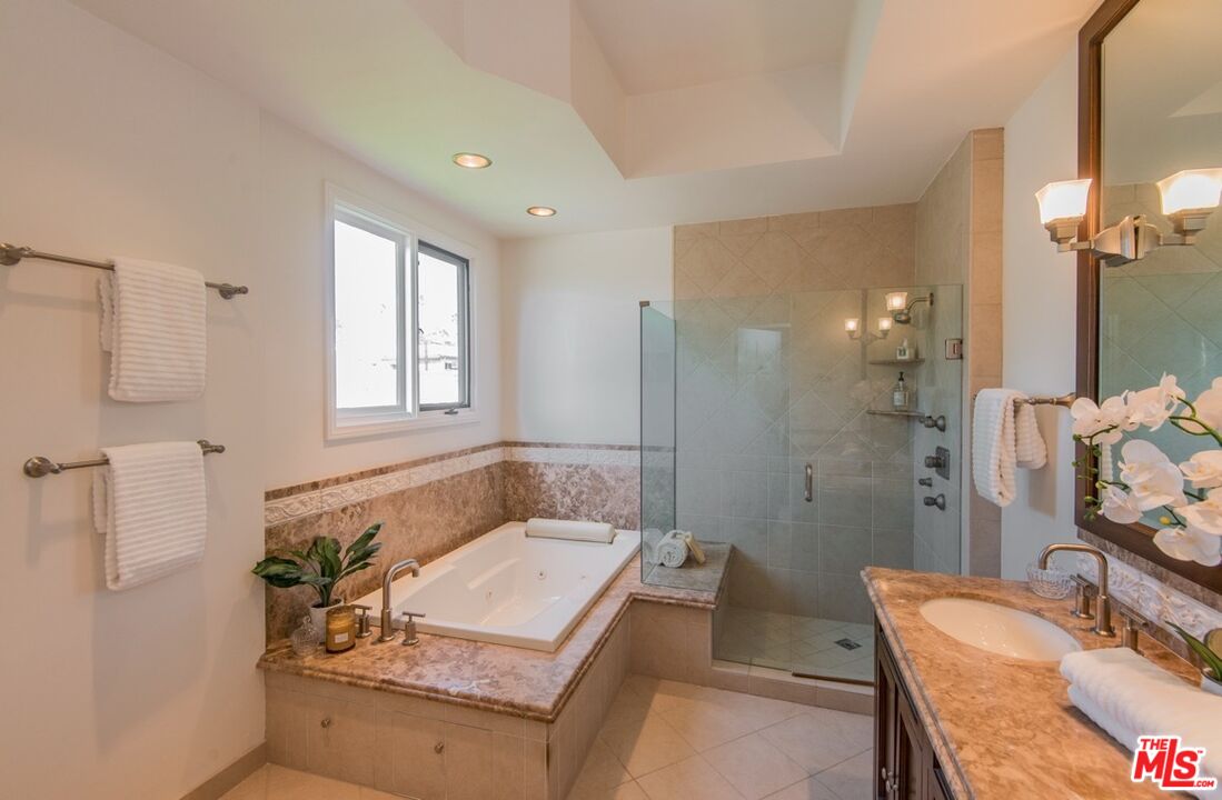 Bathroom with corner soaking tub, glass-enclosed shower, and marble vanity.