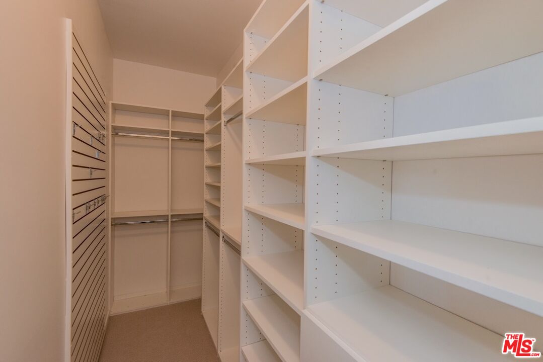 Walk-in closet with built-in white shelving, hanging rods, and slatted wall storage panels.