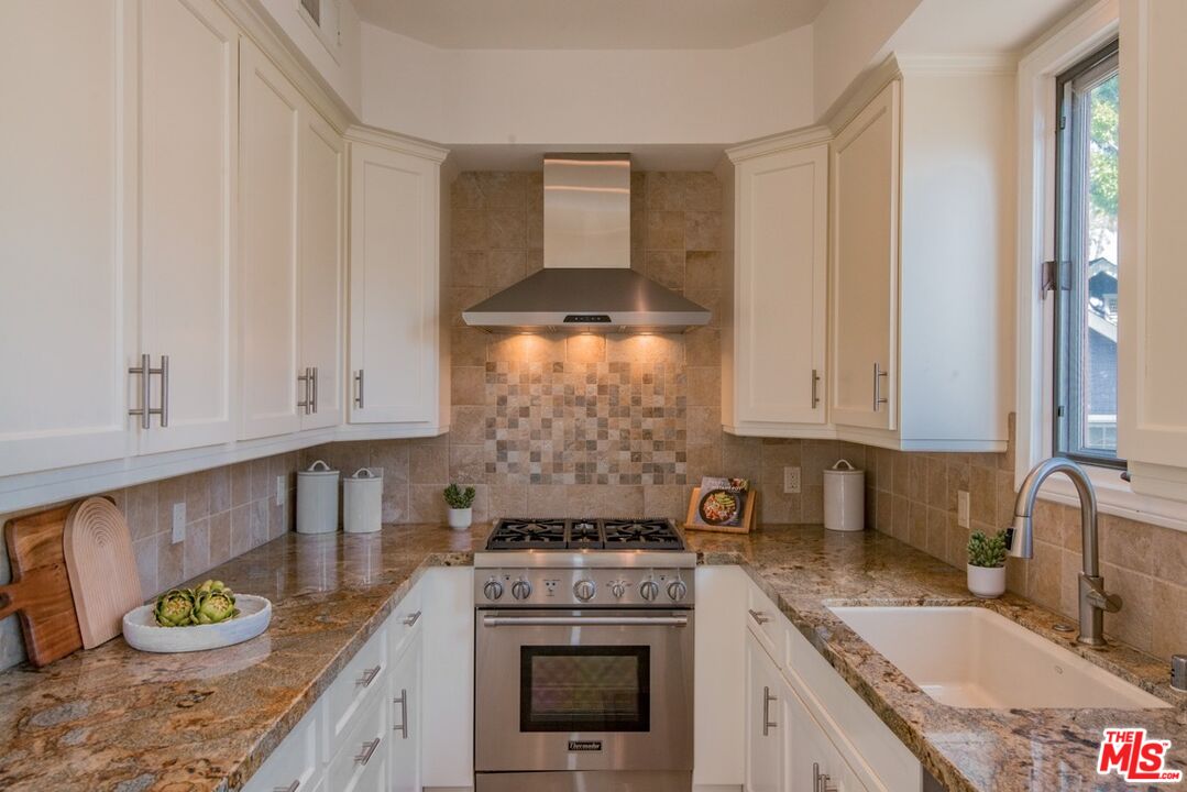 Kitchen with white cabinets, stone counters, stainless steel range, and farmhouse sink.