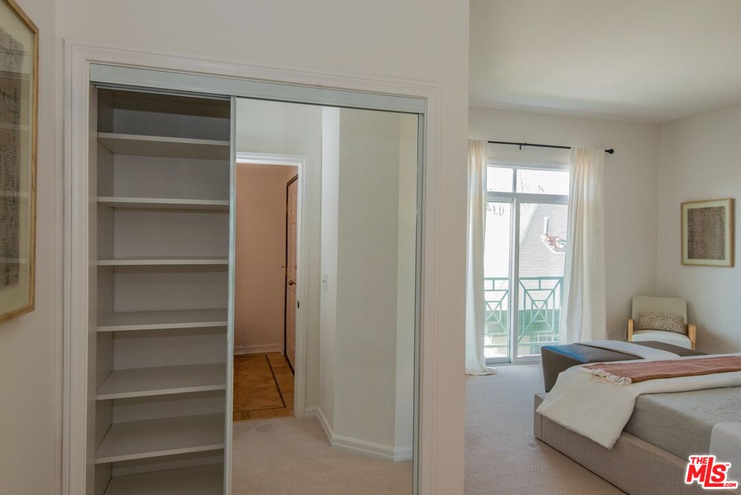 Furnished bedroom with open built-in closet shelving and glass doors to a balcony.