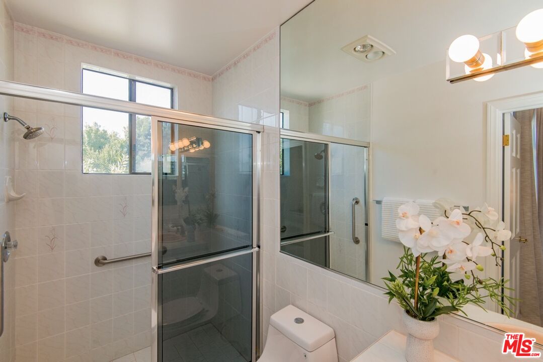 Bathroom with a glass-enclosed tiled shower, large mirror, and orchid on the vanity.