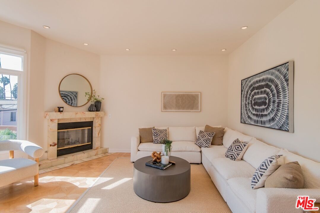 Living room with a white sectional, marble fireplace, and sunlight on parquet flooring.