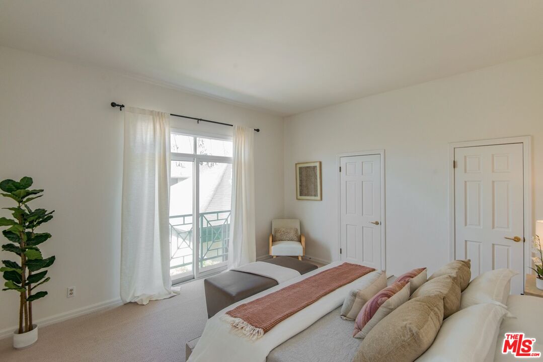 Furnished bedroom with a neutral bed, rust-colored throw, and sliding glass door to a balcony.