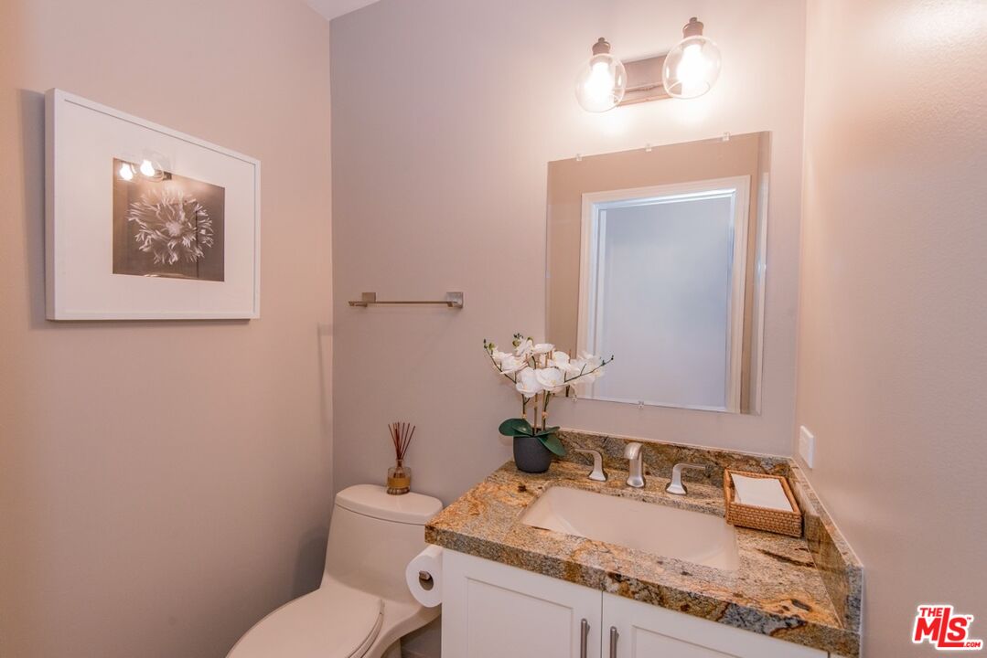 Staged bathroom with a granite vanity, large mirror, and toilet.