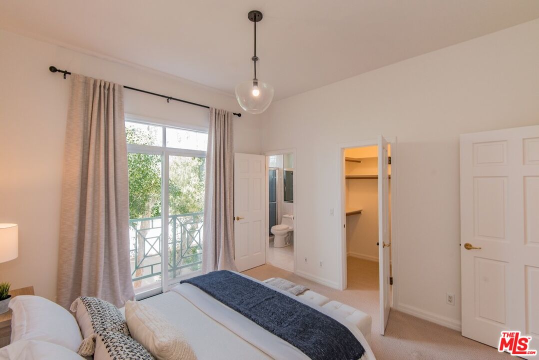 Bedroom with a curtained balcony door, a blue throw on the bed, and open bathroom and closet doors.
