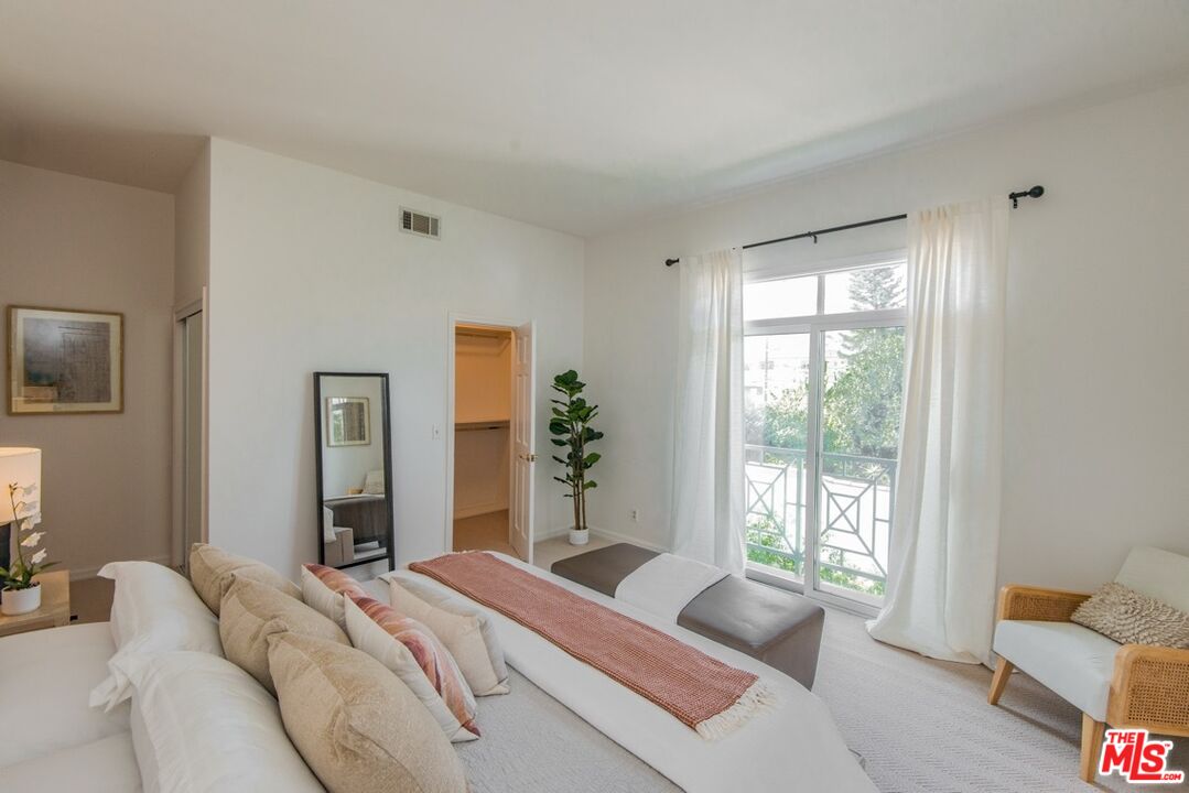 Staged bedroom with a large bed and curtained glass doors opening to a balcony.