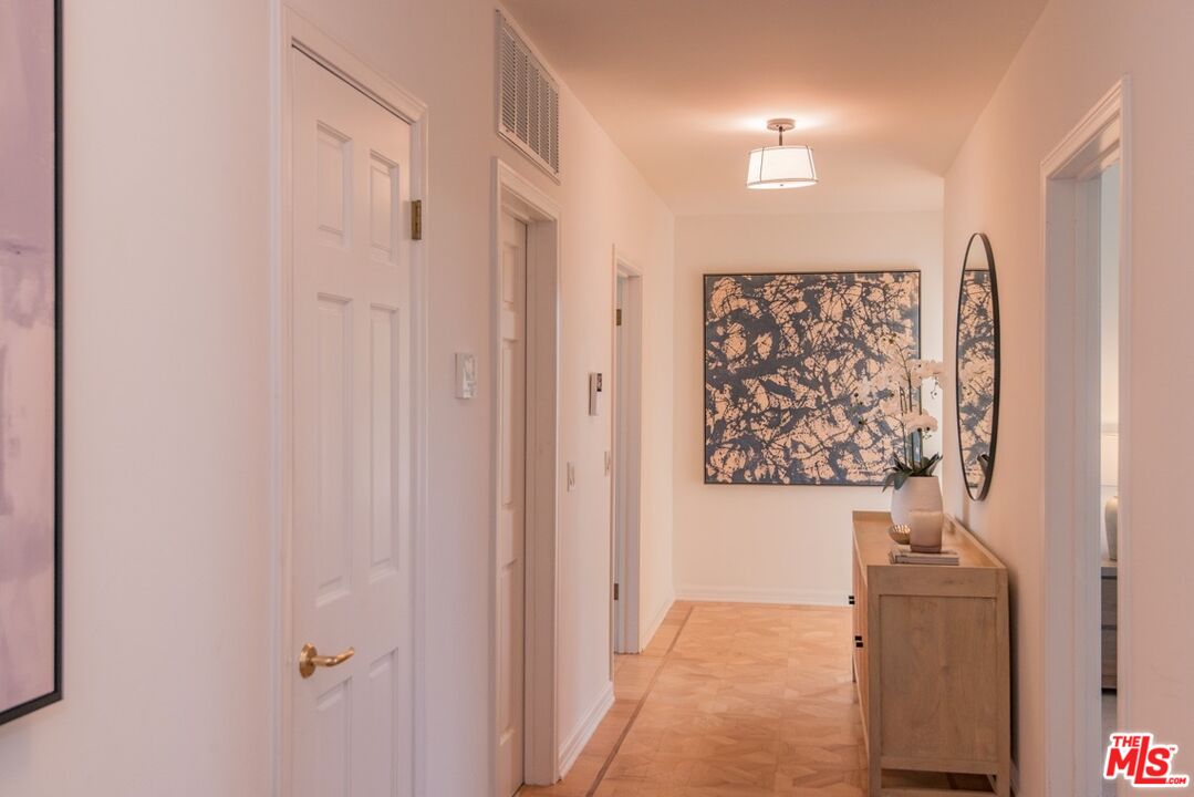Furnished apartment hallway with a wood console, orchid, oval mirror, and abstract wall art.