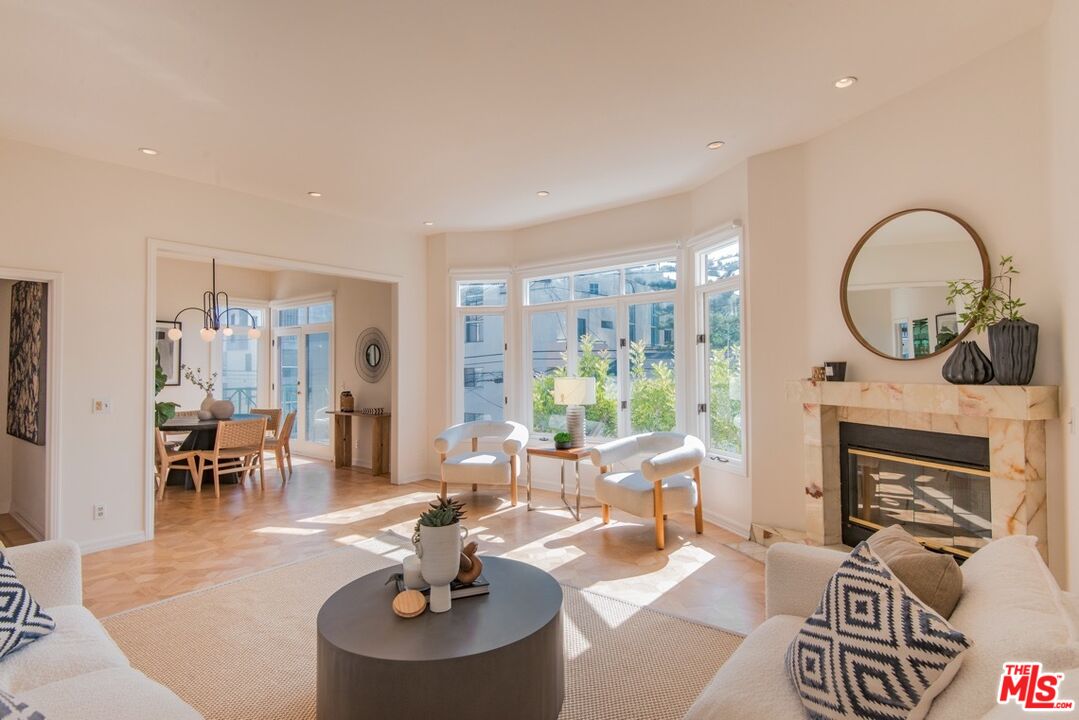 Bright living room with a marble fireplace, bay windows, and an adjoining dining area.