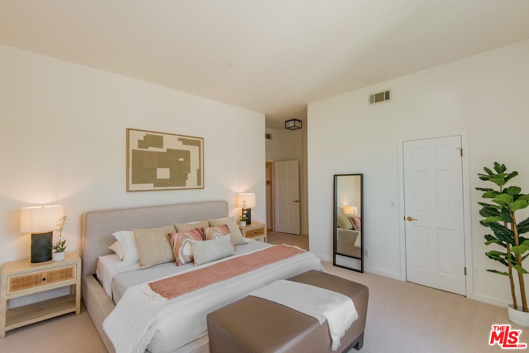 Staged bedroom with a king-size bed, abstract wall art, floor mirror, and potted plant.