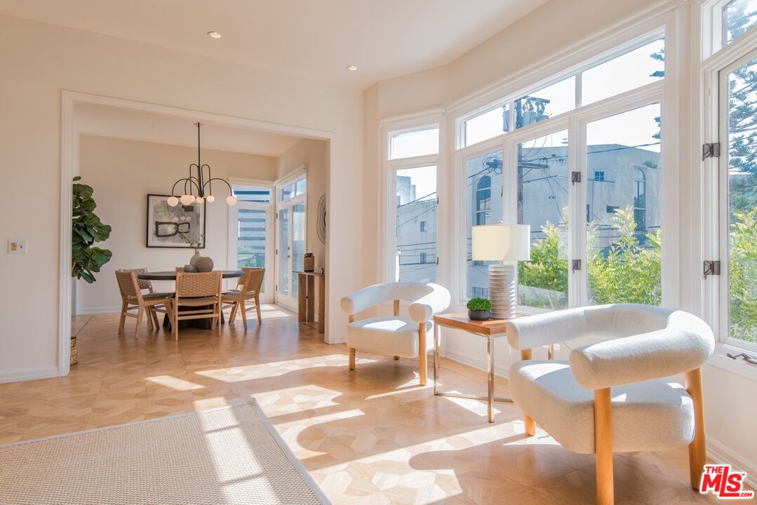 Sunlit living room with curved white chairs, parquet floors, and an adjoining dining area.