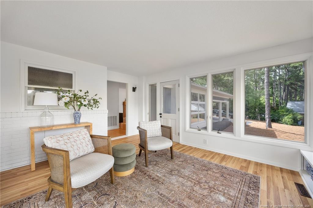Bright sitting room with large windows overlooking trees and two wicker chairs on a patterned rug.