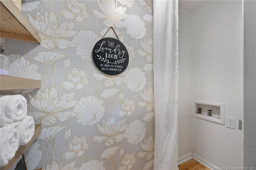 Laundry room with floral wallpaper, a round sign, open wooden shelves, and recessed wall taps.