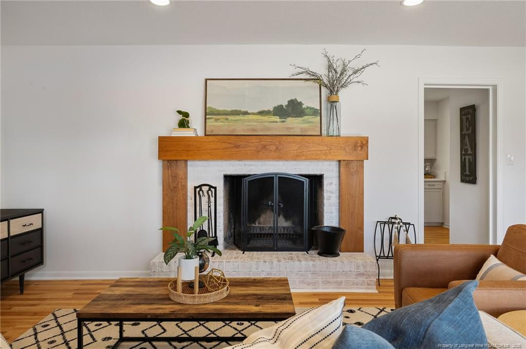 Living room with a white brick fireplace, broad wood mantel, and seating around a coffee table.