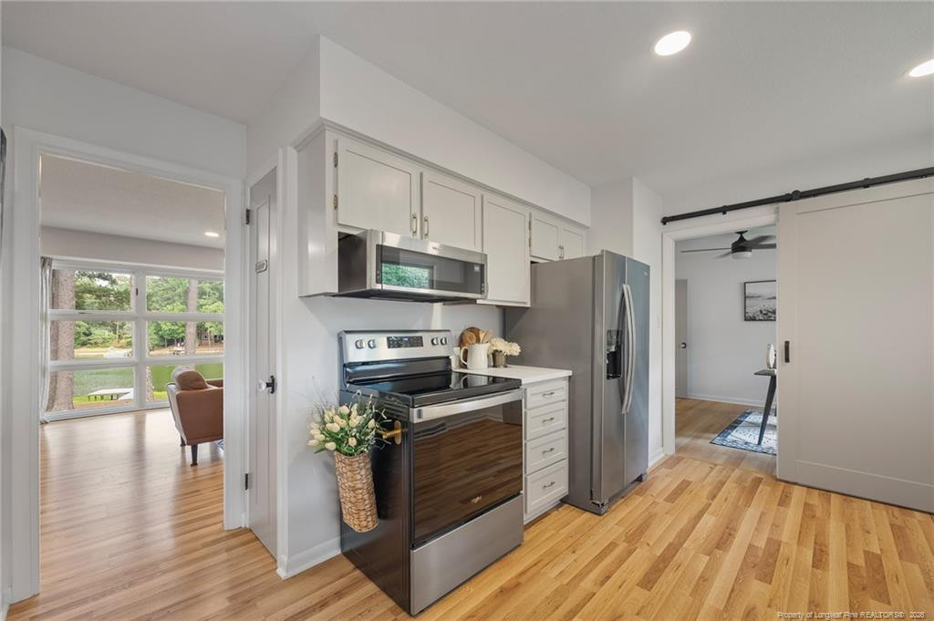 Kitchen with white cabinets, stainless steel appliances, and hardwood floors opening to a bright sitting room.