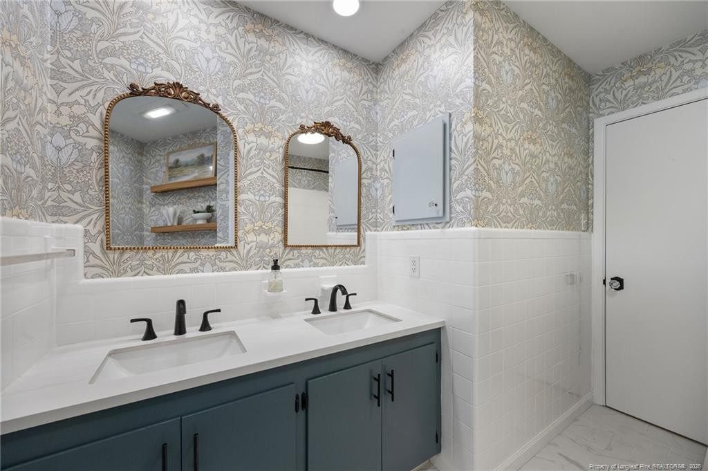 Bathroom with a blue-gray double vanity, ornate mirrors, and floral wallpaper.