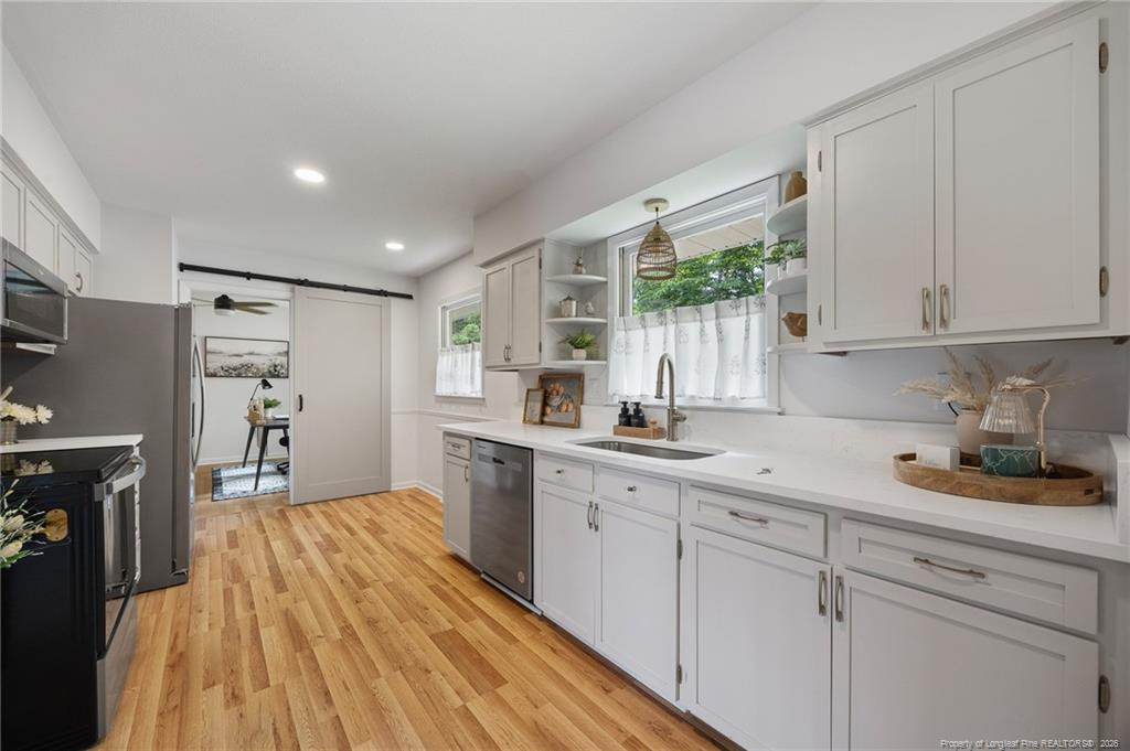Bright white kitchen with stainless-steel appliances, a curtained window, and warm wood floors.
