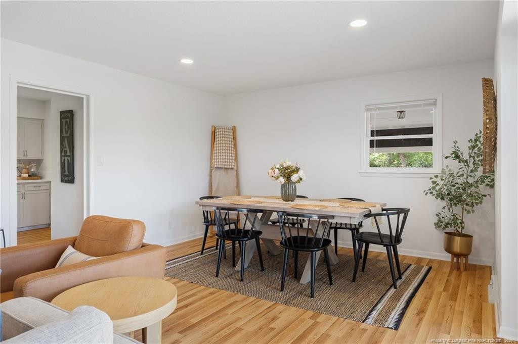 Dining room with a black chair set, woven rug, and hardwood floors beside a tan sofa.