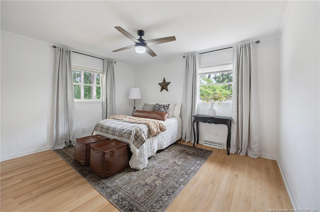 Staged bedroom with a white bed, plaid bedding, two curtained windows, and a dark ceiling fan.