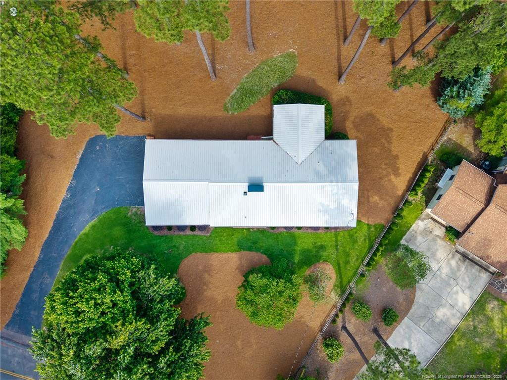 Aerial view of a single-story home with a white roof, curved driveway, and mature trees.