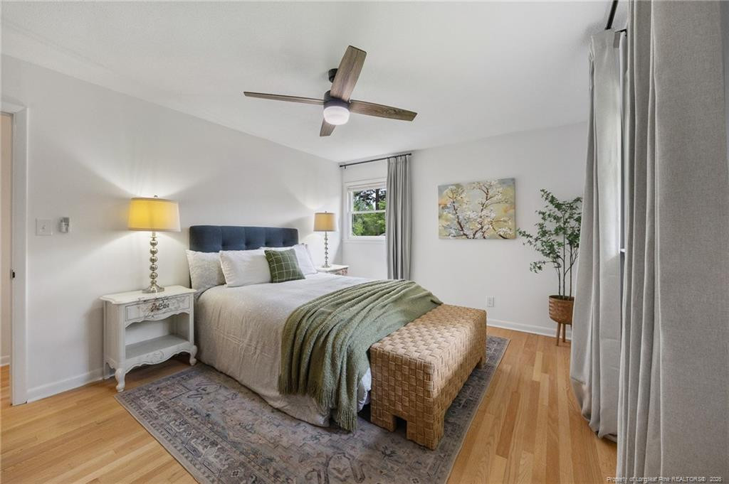 Furnished bedroom with a green throw, woven bench, hardwood floors, and ceiling fan.