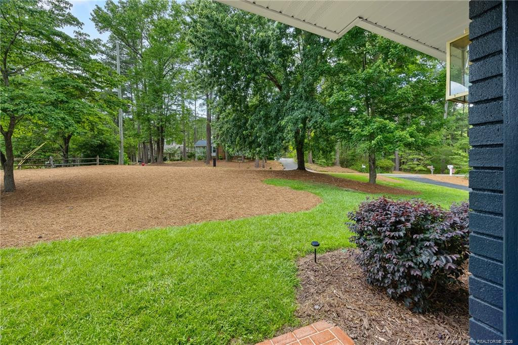 Landscaped yard with green lawn, mature trees, and a broad mulched area, viewed from a covered porch.
