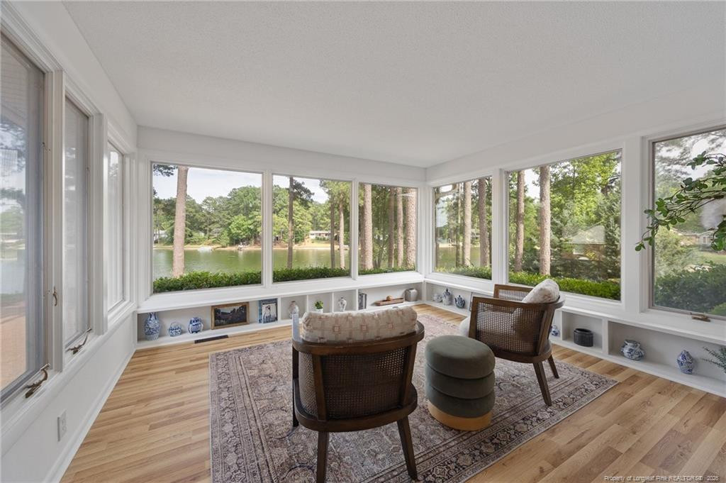 Sunroom with wide windows overlooking a lake, built-in display shelves, and two chairs.