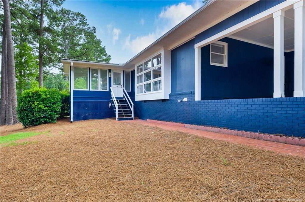 Blue house with a covered porch and white-trimmed steps beside a pine-straw yard.