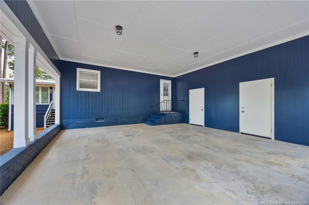 Covered patio with a concrete floor, dark blue siding, and steps to a white door.