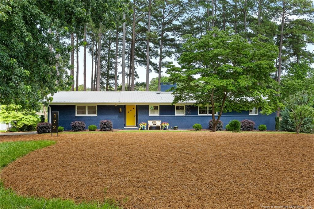 Blue single-story house with a yellow front door, metal roof, and pine-straw lawn.