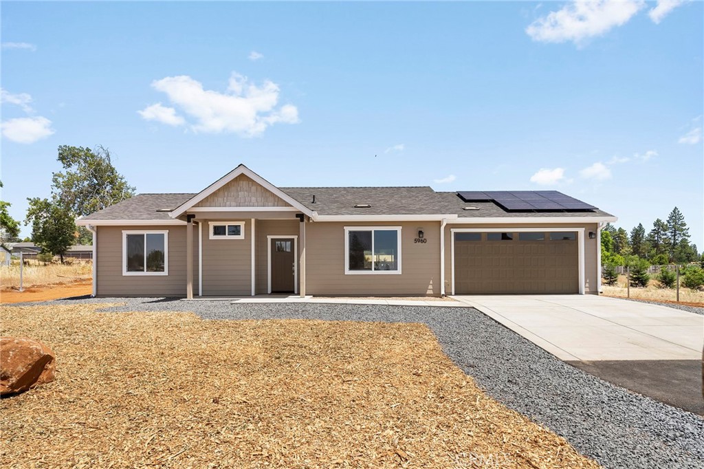 Single-story beige home with a covered porch, two-car garage, and rooftop solar panels.