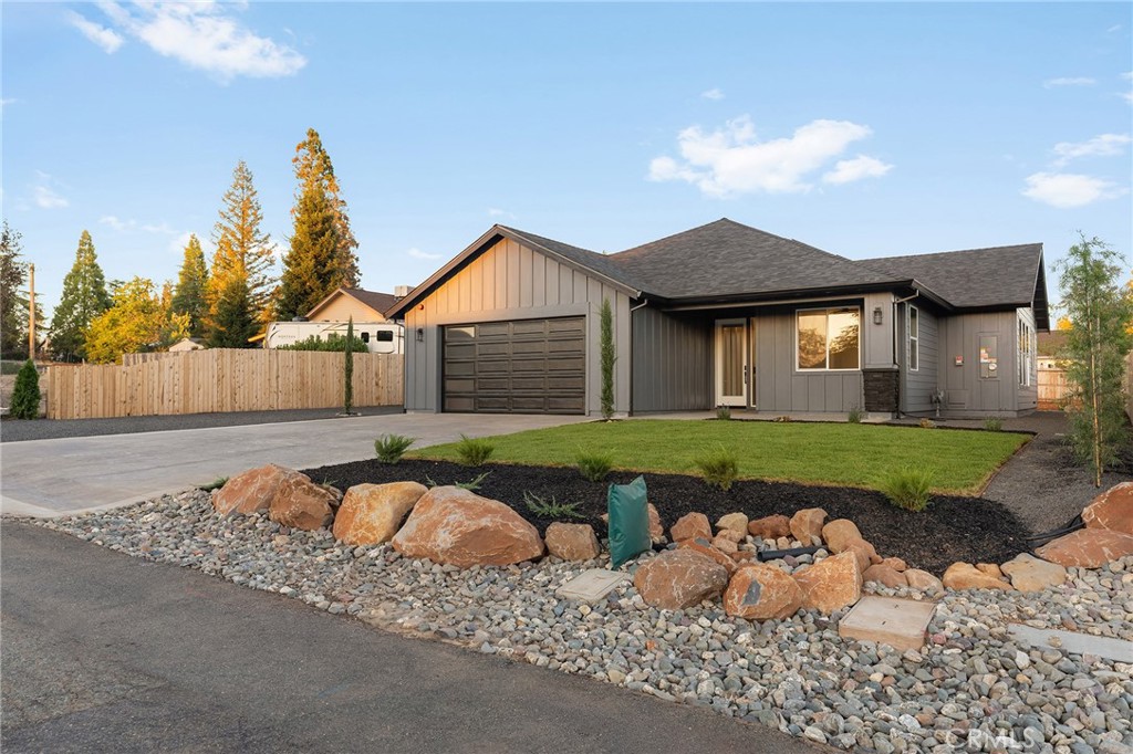 Gray single-story home with an attached double garage, fenced side yard, and landscaped rock beds.