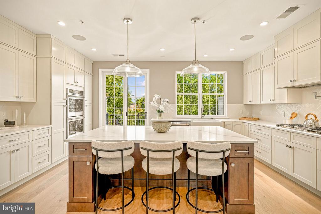 Bright kitchen with white cabinetry, a large wood island, three bar stools, and windows overlooking trees.